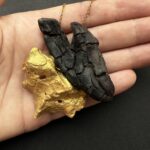 Colgante artesanal creado con madera del mar traida por las mareas y oscura y agrietada en forma de corazón y concha de ostra dorada. cadena dorada de acero inoxidable.