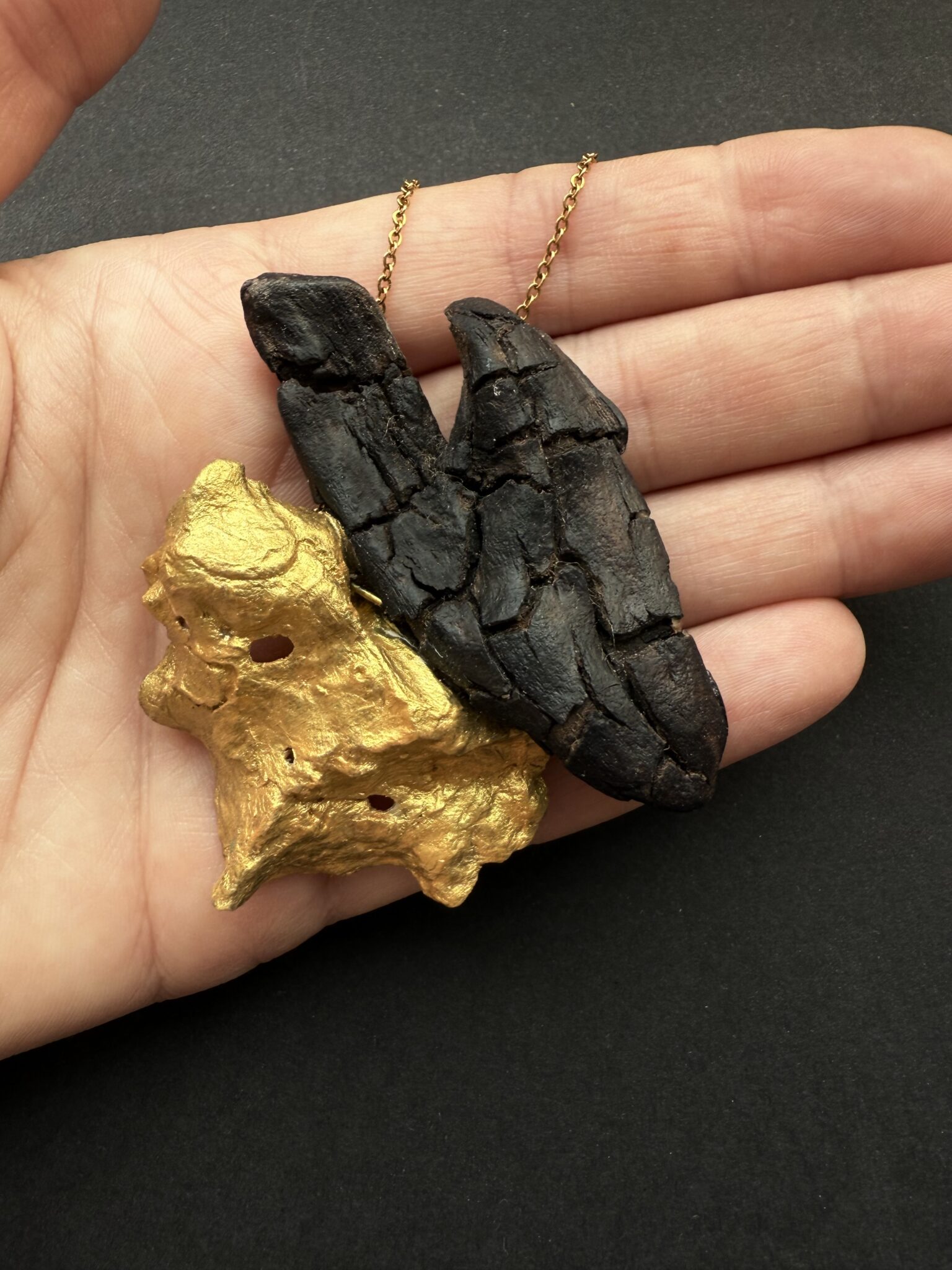 Colgante artesanal creado con madera del mar traida por las mareas y oscura y agrietada en forma de corazón y concha de ostra dorada. cadena dorada de acero inoxidable.