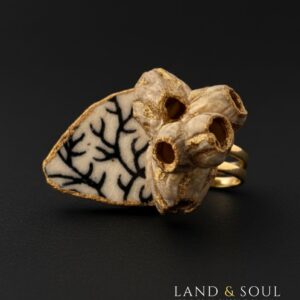 «Anillo artesanal con barnacles y cerámica marina negra, pieza única de Land & Soul sostenida con la mano»